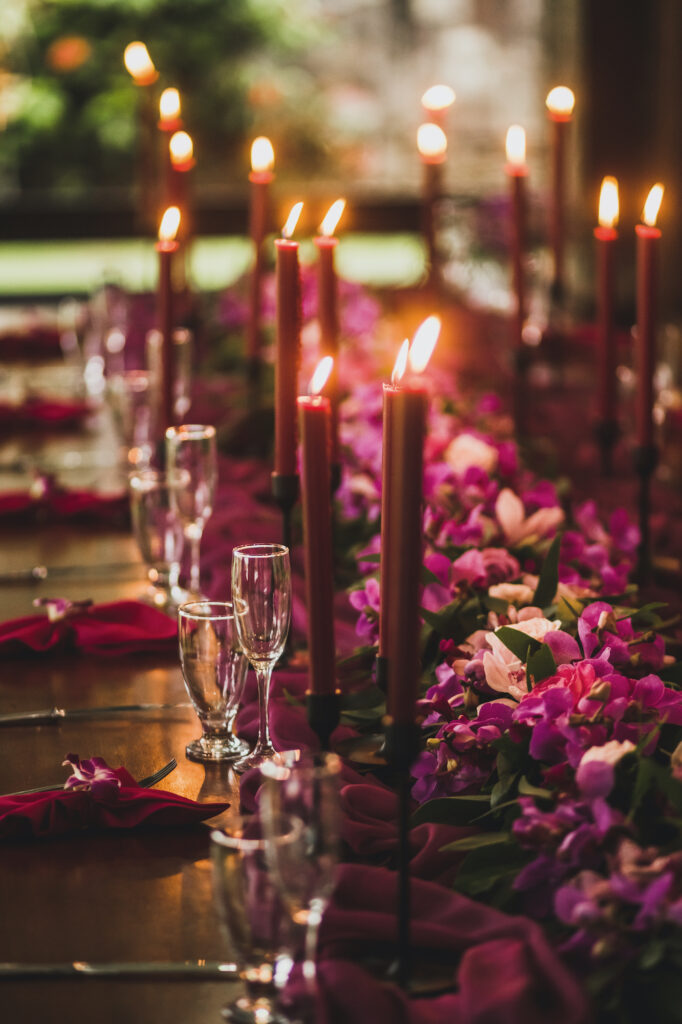 Wooden wedding table decorated with red candles, pink cloth and purple orchids. Romantic family dinner in evening