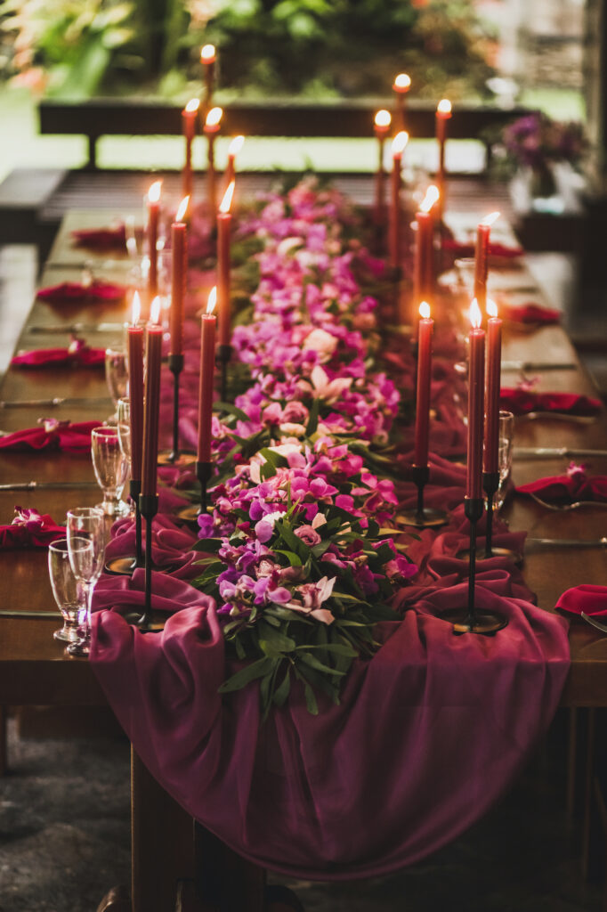 Wooden wedding table decorated with red candles, pink cloth and purple orchids. Romantic family dinner in evening